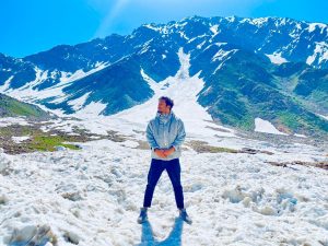 Traveler standing on a snowy mountain landscape with towering snow-capped peaks and a clear blue sky in the background.