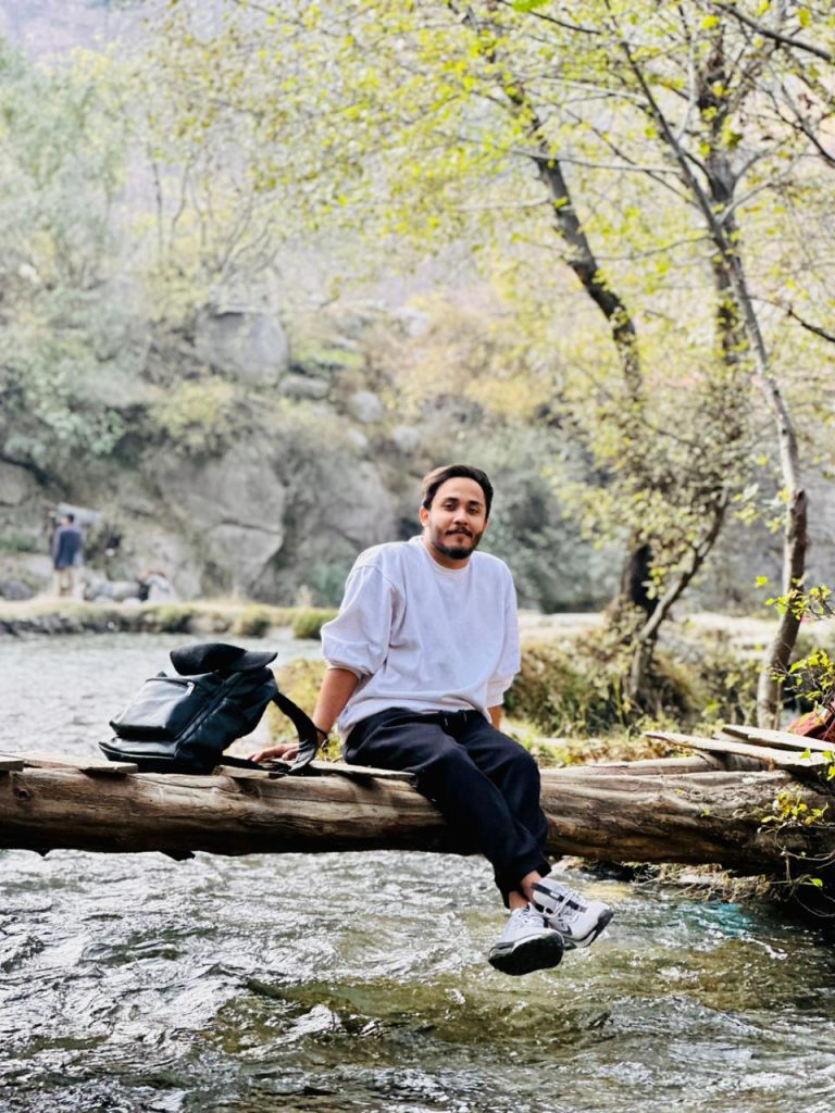 Traveler sitting on a wooden log beside a flowing river surrounded by trees and nature
